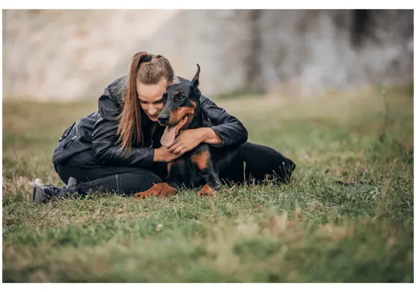 A lady leaning on her Doberman